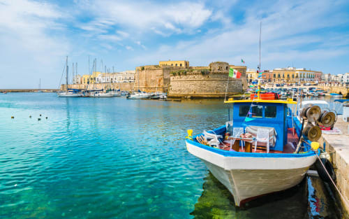 Barca da pesca colorata nel porto di Torre Lapillo con forte storico e barche a vela, Italia