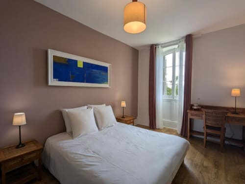 Modern bedroom suite at Domaine du Faure B&B with white bedding, mauve walls, blue artwork, garden view doors, and warm