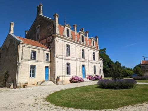 Façade extérieure du Domaine du Faure à Chadurie, pierre beige, toit en terre cuite, portes bleues, lavande et fleurs roses