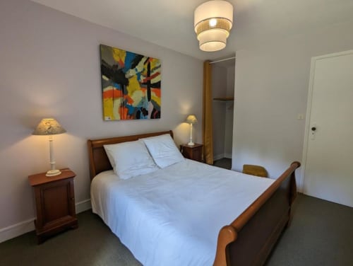 Chambre lumineuse au Domaine du Faure avec lit en bois, linge blanc, lampes de chevet, œuvres d'art colorées et vue sur le jardin