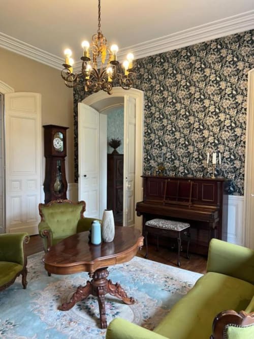 Élégant salon au Domaine du Faure avec fauteuils en velours vert, lustre orné, piano noir et papier peint damassé
