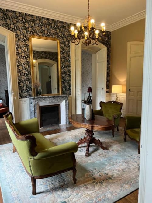 Élégant salon du Domaine du Faure avec papier peint damassé, fauteuils velours vert, miroir orné, lustre et cheminée