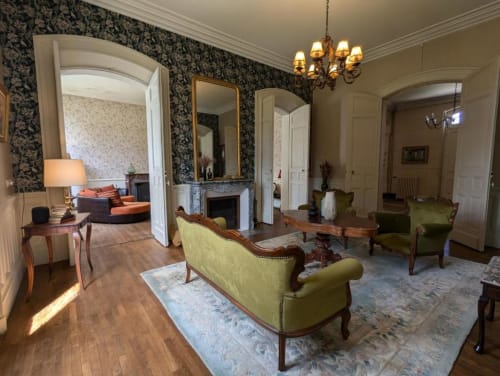 Élégant salon de la suite Domaine du Faure avec fauteuils tapissés vert, cheminée, papier peint damassé et parquet.