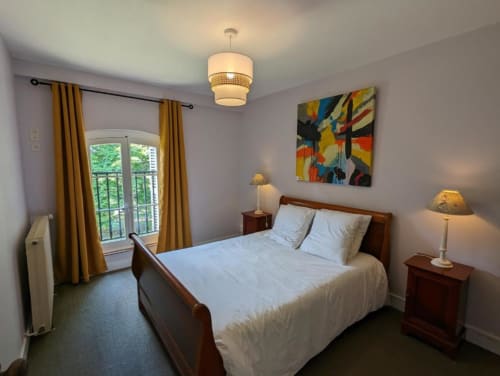 Chambre au Domaine du Faure avec lit en bois, vue jardin par portes-fenêtres, rideaux dorés et tableaux colorés
