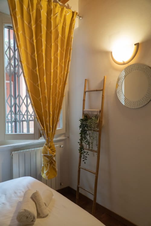 Camera da letto accogliente della Naviglio Grande Suite a Torino, con tende dorate, libreria a scala in legno con piante e specchio rotondo
