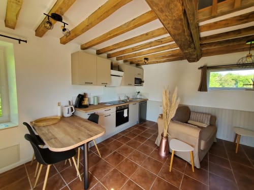 Cuisine et salle à manger du gîte au Clos Des Sources, Isigny-sur-Mer avec poutres en bois, cuisine équipée et vue sur le jardin