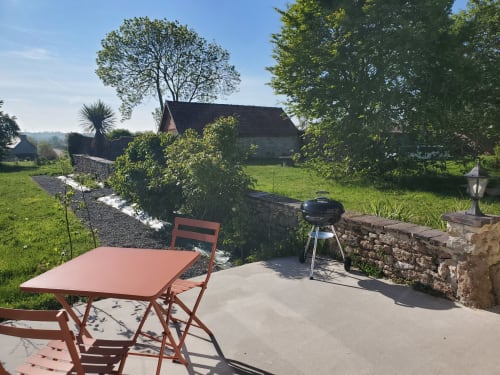 Terrasse de jardin charme au gîte Le Clos Des Sources à Isigny-sur-Mer avec table rustique, barbecue et maison en pierre