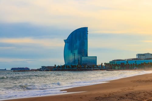Edificio azul curvo en la playa de Barcelona con olas y arena al atardecer, hotel Apartamenting SL
