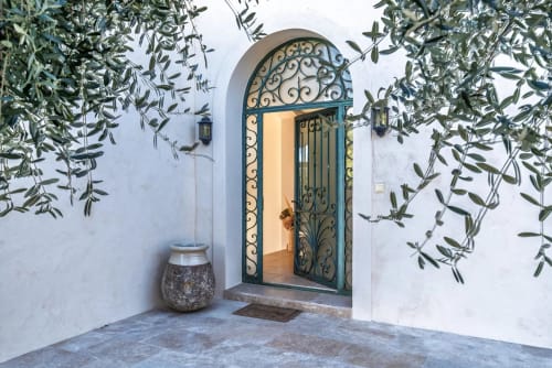 Elegant arched doorway with ornate ironwork at M Résidences villa in Cannes-Mougin, framed by cascading olive branches