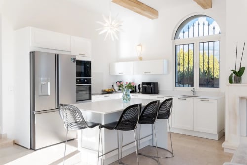 Modern villa kitchen with white cabinetry, stainless steel appliances, island seating for 3, and arched windows overlooking
