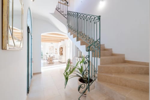 Modern villa staircase with ornate wrought iron railing and terracotta steps, leading to bright open living area in