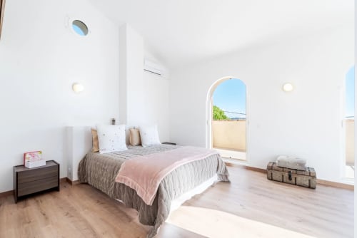 Bright modern bedroom in Cannes villa with bed, wood flooring, arched door opening to terrace with pool view