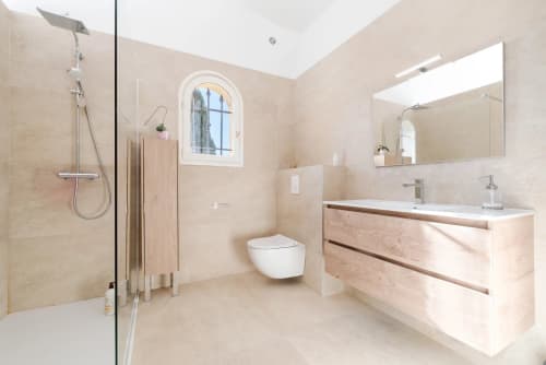 Modern luxury bathroom in Cannes villa with walk-in shower, double vanity, and natural light from arched window