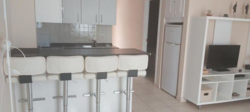 Moderna cocina y sala de estar en Smart Rent Fuerteventura con muebles blancos, barra y televisor de pantalla plana