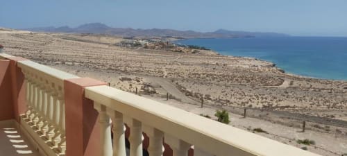Vista desde terraza de balcón de la costa de Fuerteventura con océano turquesa, paisaje desértico y resort lejano