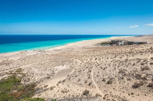 Vista aérea de Smart Rent Fuerteventura frente al mar con aguas turquesas, playa de arena y paisaje desértico en La Palma