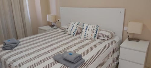 Dormitorio luminoso en Smart Rent Fuerteventura con ropa de cama a rayas, almohadas decorativas y modernos mesitas blancas