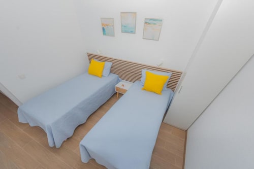 Habitación doble con ropa de cama azul y almohadas amarillas en Smart Rent Fuerteventura, con cabecero de madera y arte costero.