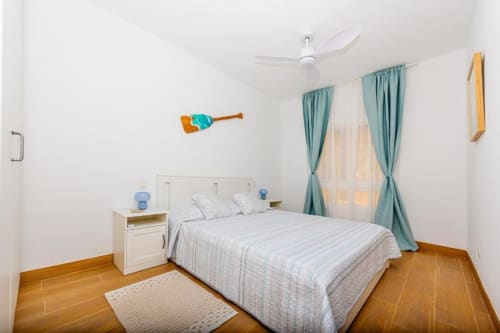 Dormitorio luminoso en apartamento Brisa del Atlántico de Smart Rent Fuerteventura con cama queen, cortinas turquesas y piso de madera