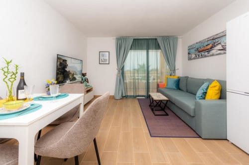 Moderno salón de apartamento con mesa de comedor, sofá gris, cocina y balcón con vistas al mar en Smart Rent Fuerteventura