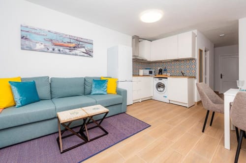 Sala de estar del apartamento Brisa del Atlántico con sofá turquesa, cocina, lavadora y mobiliario moderno en Smart Rent