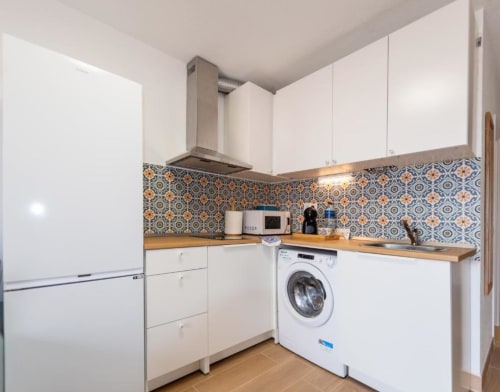 Cocina moderna en apartamento Brisa del Atlántico con gabinetes blancos, lavadora, backsplash con azulejos geométricos azules