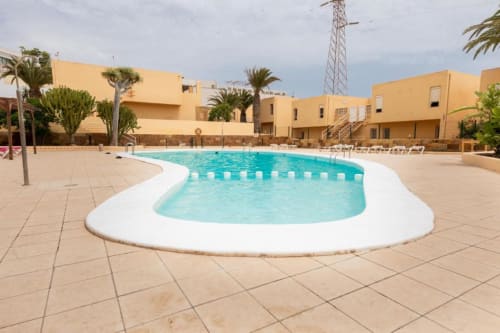 Piscina riñón con agua turquesa en el resort villa Smart Rent Fuerteventura, rodeada de baldosas beige