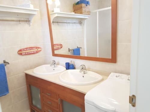 Baño moderno con dos lavabos, tocador de madera, espejo y decoración náutica en apartamento Casa Storm de Smart Rent