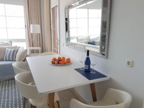 Zona de comedor moderna en apartamento Casa Storm con mesa blanca, naranjas frescas, botella de vino y vistas al océano desde el balcón