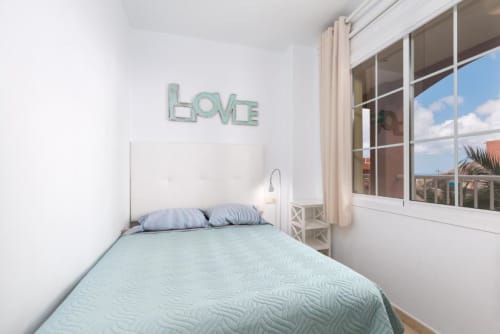 Dormitorio luminoso en Casa Storm, apartamento en Fuerteventura con vista al océano, cama queen, almohadas a rayas y letrero de neón LOVE