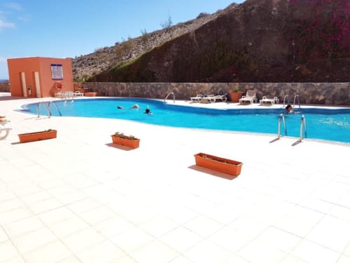 Piscina del complejo con agua turquesa, tumbonas e instalaciones naranjas junto a una ladera rocosa en Smart Rent
