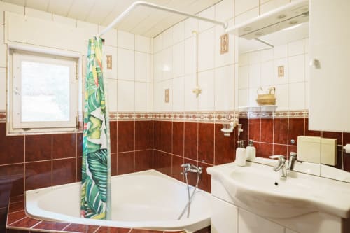 Bathroom in Gank Apartment at Kmetija Pečnik, Prevalje with brown tile walls, white bathtub, sink, and window view