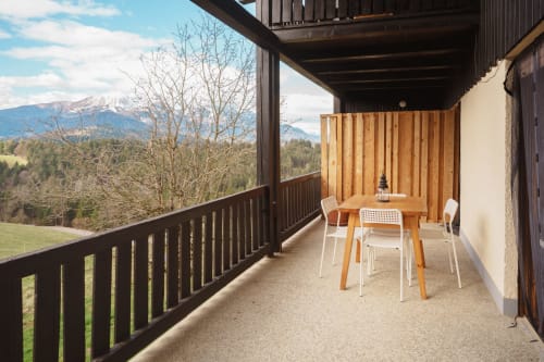 Mountain view terrace at Kmetija Pečnik in Prevalje with wooden dining table, chairs, and alpine scenery in background