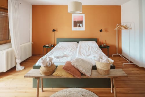 Modern bedroom at Kmetija Pečnik in Prevalje with orange accent wall, queen bed, wooden floors, and mountain view window.