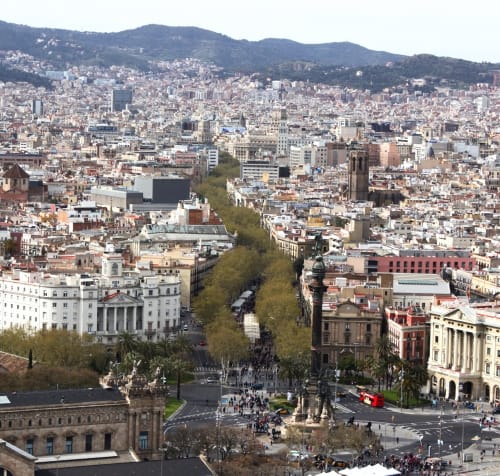Paisaje urbano de Barcelona con avenida arbolada, edificios históricos y montañas de fondo - Apartamenting SL