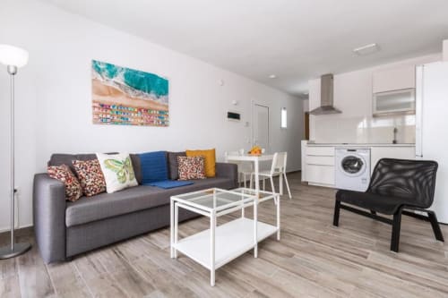 Apartamento moderno en Smart Rent Fuerteventura con sofá gris, zona de comedor, cocina y lavadora en salón abierto