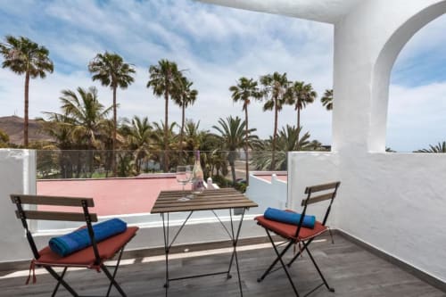 Zona de descanso en la terraza de Smart Rent Fuerteventura con palmeras, plataforma de piscina rosa y vistas al océano en Tarajalejo