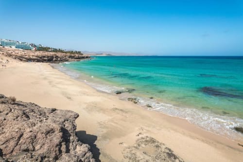 Playa virgen con aguas turquesas y arena dorada en Smart Rent Fuerteventura, Tarajalejo. Cielo azul despejado y costa rocosa