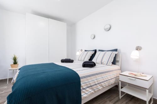 Dormitorio moderno con ropa de cama turquesa, almohadas a rayas, armario blanco y vista al jardín en apartamento Smart Rent Fuerteventura