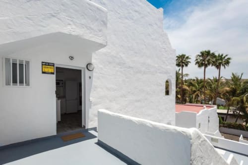 Exterior de apartamento blanco con vistas al jardín en Smart Rent Fuerteventura, palmeras visibles, cielo azul, entrada a la terraza