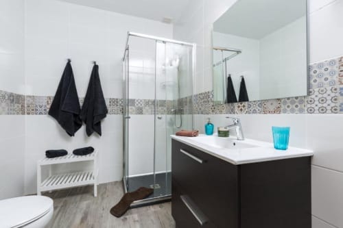 Baño moderno con tocador negro, lavamanos blanco, mampara de ducha, azulejos estampados y toallas negras en Smart Rent