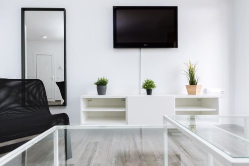 Moderno salón en Smart Rent Fuerteventura con televisor de pantalla plana, estanterías blancas, plantas y vistas al jardín