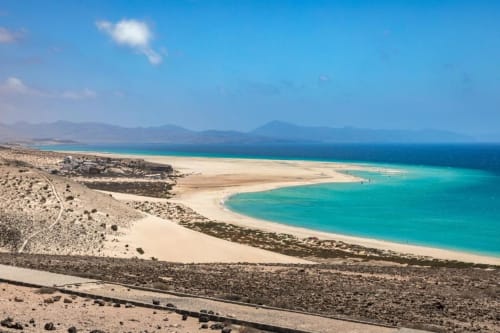 Laguna turquesa con playa de arena blanca y paisaje árido en Fuerteventura, España