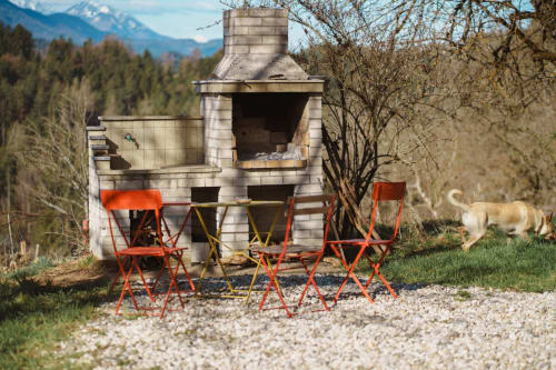 Rustic outdoor fireplace with red camping chairs and grill in mountain valley setting at Kmetija Pečnik, Slovenia