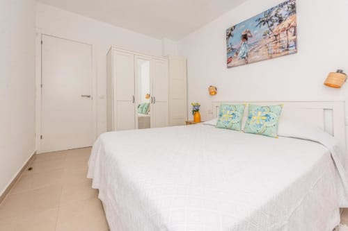 Dormitorio luminoso en Smart Rent Fuerteventura con cama blanca, almohadas verdes, armario y decoración temática playera en la Casa de Alex