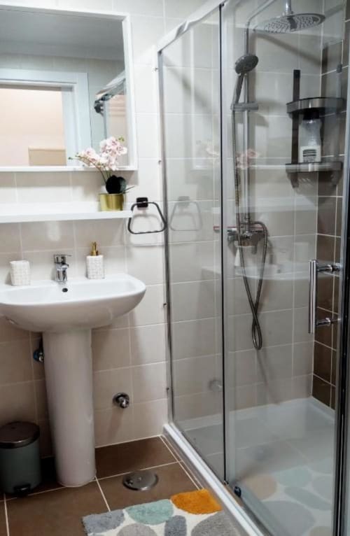 Baño moderno con lavabo pedestal, ducha con mampara de cristal y paredes revestidas de azulejos blancos en el apartamento Alex's House de Fuerteventura