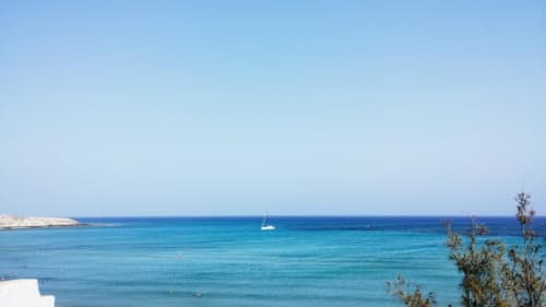 Aguas turquesas del Mediterráneo con velero frente a la costa de Fuerteventura, acantilados blancos y vegetación en primer plano