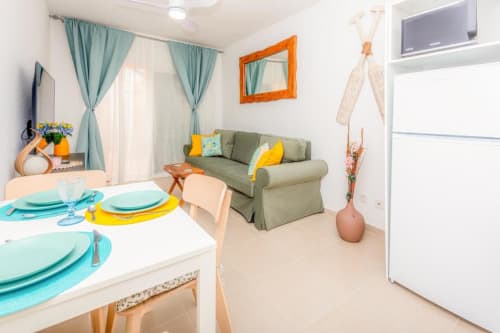 Apartamento Alex's House en Smart Rent Fuerteventura con mesa de comedor, sofá verde, cocina y detalles turquesas.