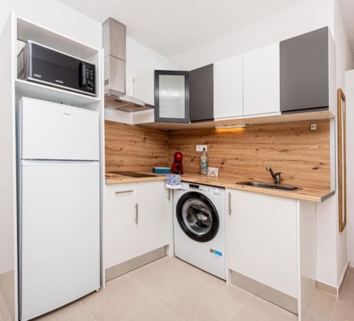 Cocina moderna con muebles blancos, encimeras de madera, electrodomésticos de acero inoxidable y lavadora en la casa de Alex