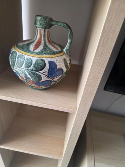 Jarra cerámica decorativa con esmalte verde y motivos de hojas azules en repisa de madera en apartamento Smart Rent Fuerteventura